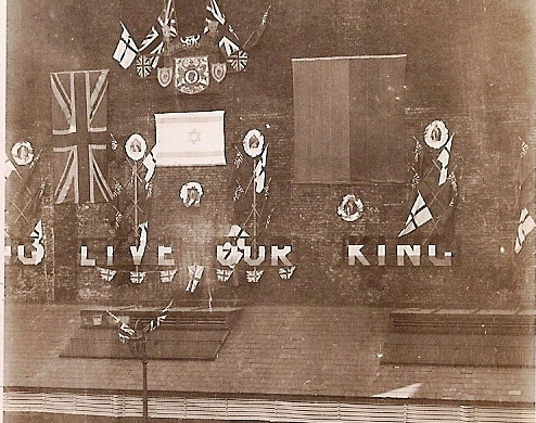 Above, decorated wall of the Netherlands club for Jews Free School's George 5th Silver Jubilee celebrations, 8 July 1935, viewed from the playground of Jews Free School, Bell Lane. The foreground shows tables laid for their celebration feast.
